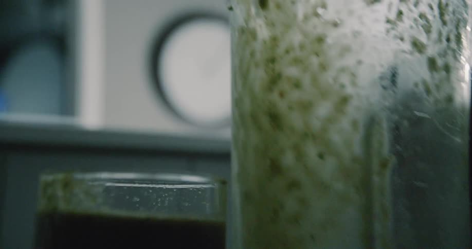 Green juice is being poured from a pitcher into a glass inside in daylight