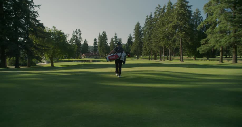 Person carrying a golf bag on a green