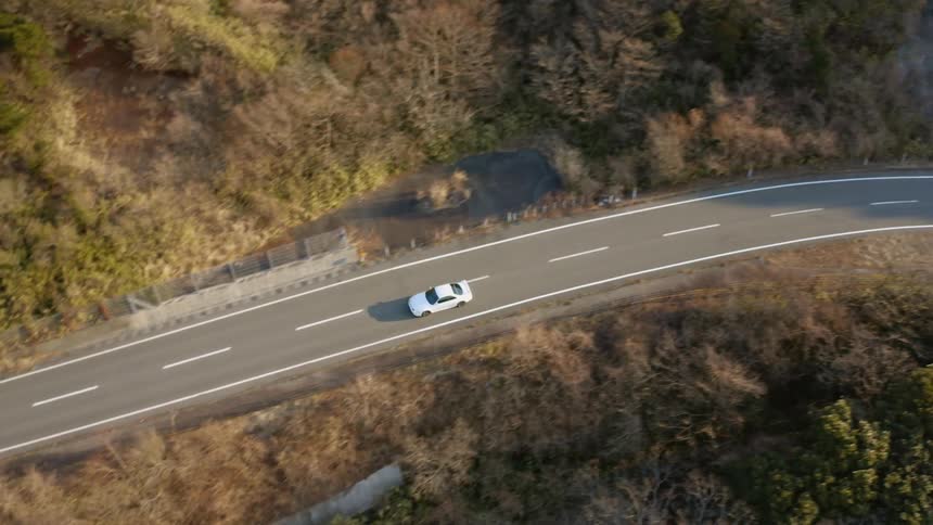 A car is driving on a road in daylight through a natural landscape