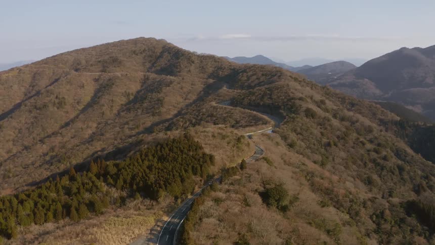 Road winding through tall grassy mountains with vehicles traveling over it