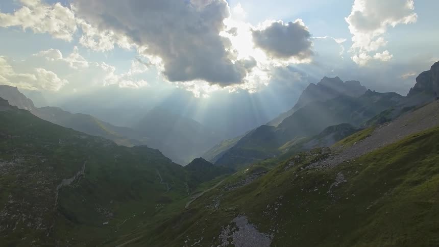 The sun is creating rays behind the clouds over the mountains
