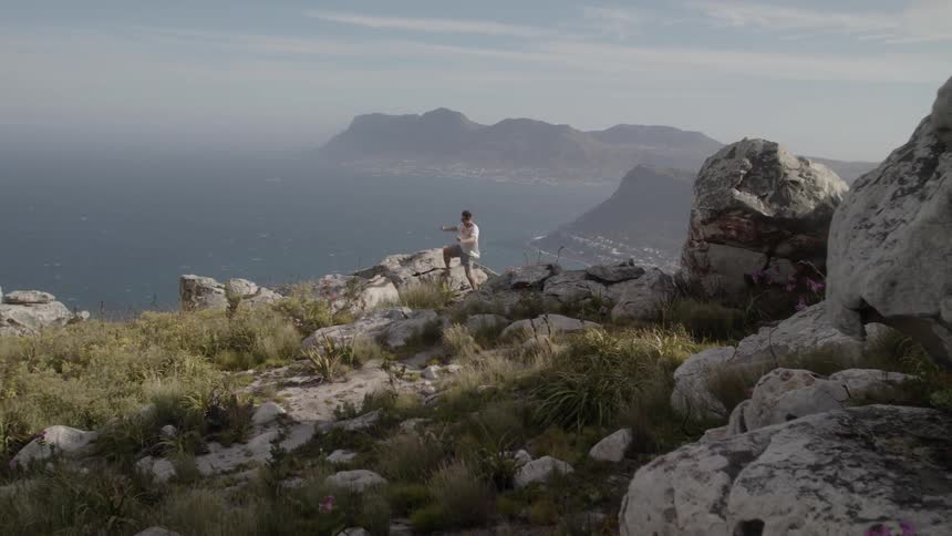 Man jumps on rocks on a hilltop overlooking water