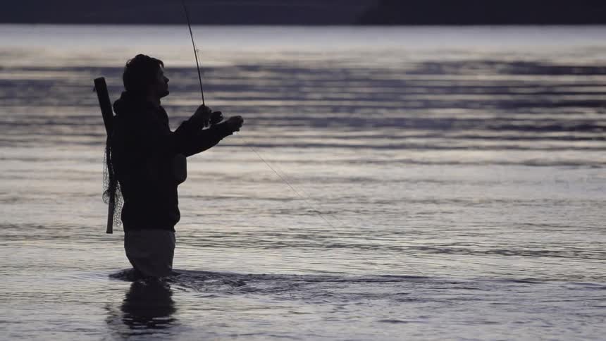 Man standing knee high in water fishing