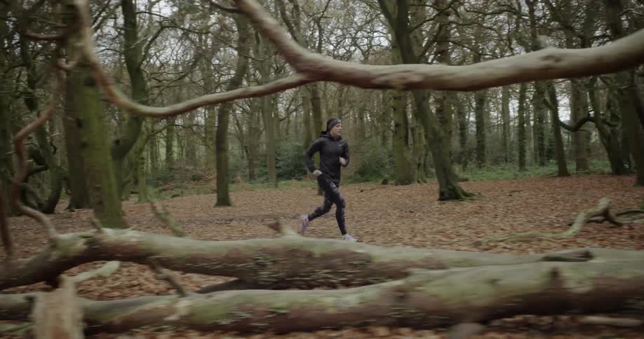 The woman is jogging through the forest