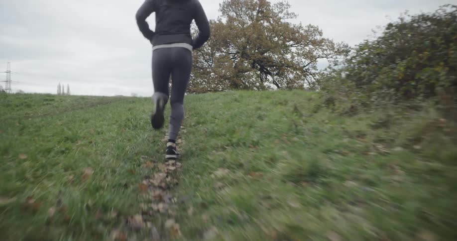 Woman jogs in a grassy field near trees