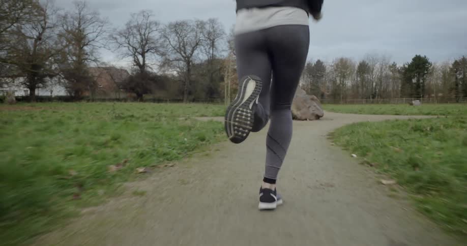 Woman jogging on dirt path through grassy field