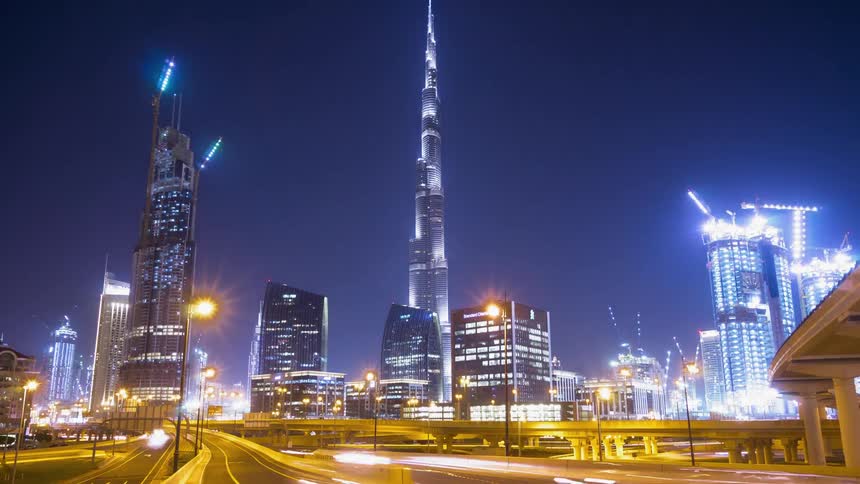 Cars speed down a highway out of a bright city at night