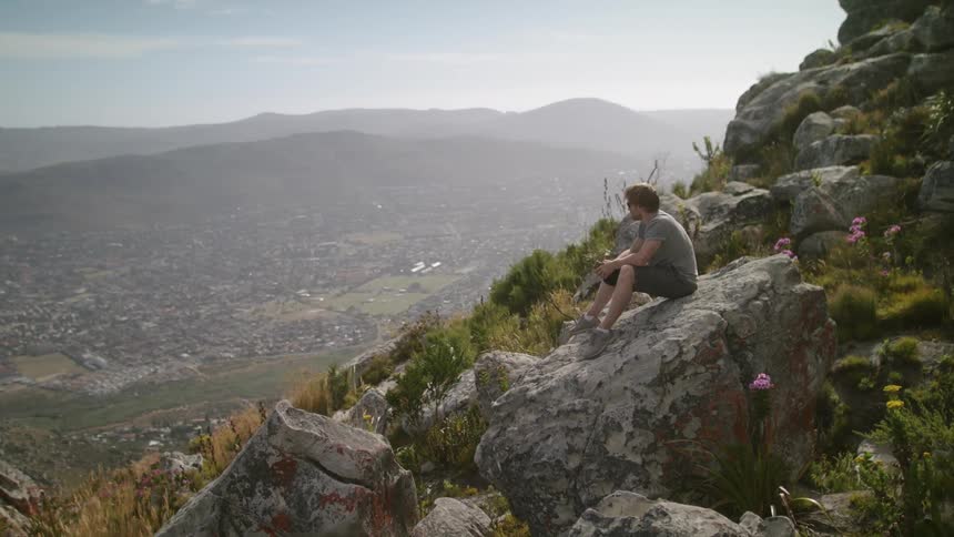 Man sits on a large rock on a mountain top on a sunny day