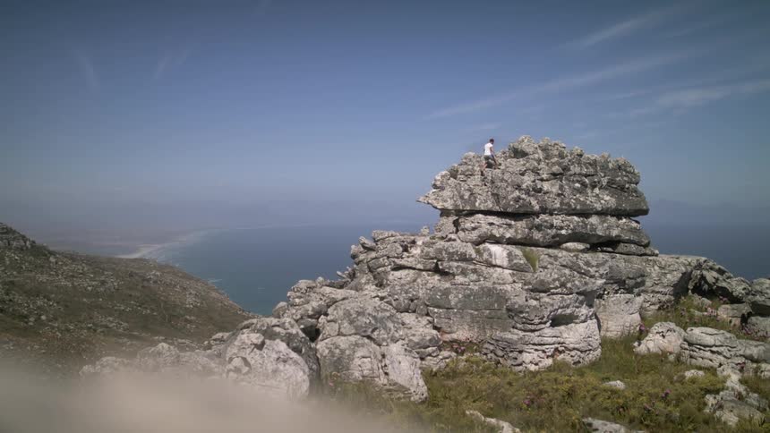 Person climbs up a large rock formation overlooking water