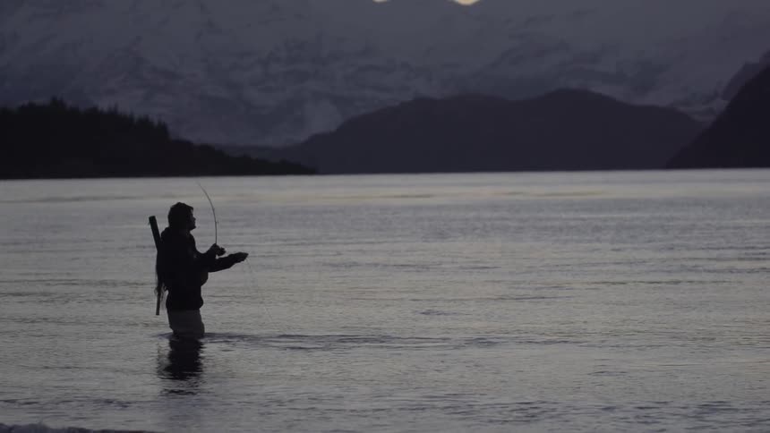 A silhouetted man fishes in a lake