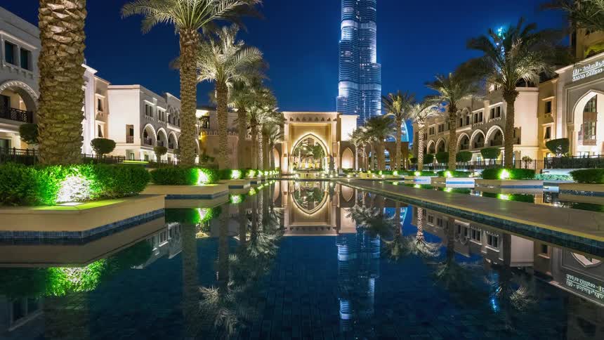 People walk around a palm tree lined pool at night