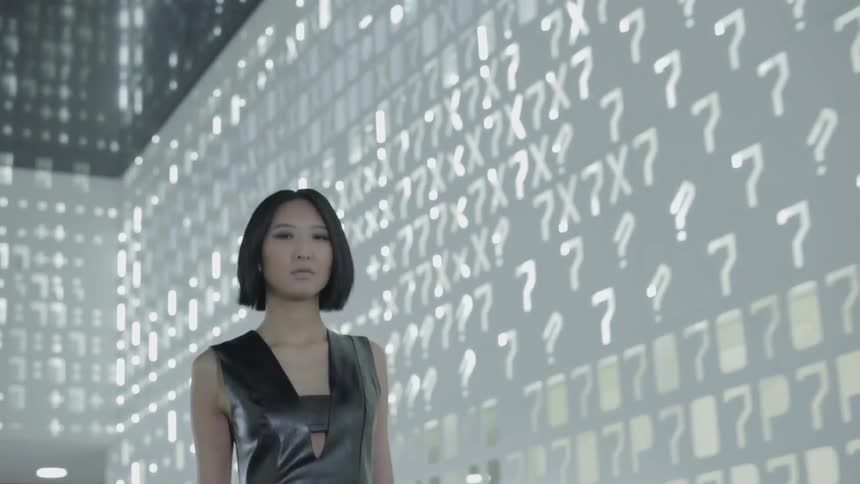 Woman walks near a wall with holes in it and light shining through