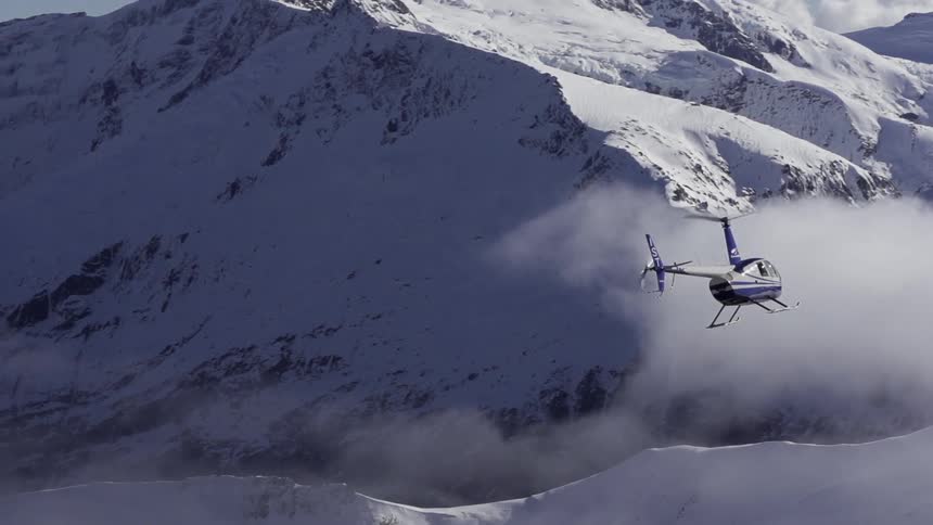 A helicopter is flying over snowy mountains