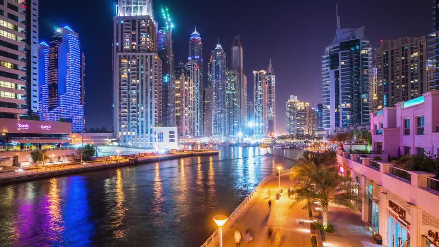 Boats are traveling on a river through an urban area at night