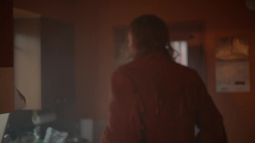 A man walks around a house and stops to look out a window