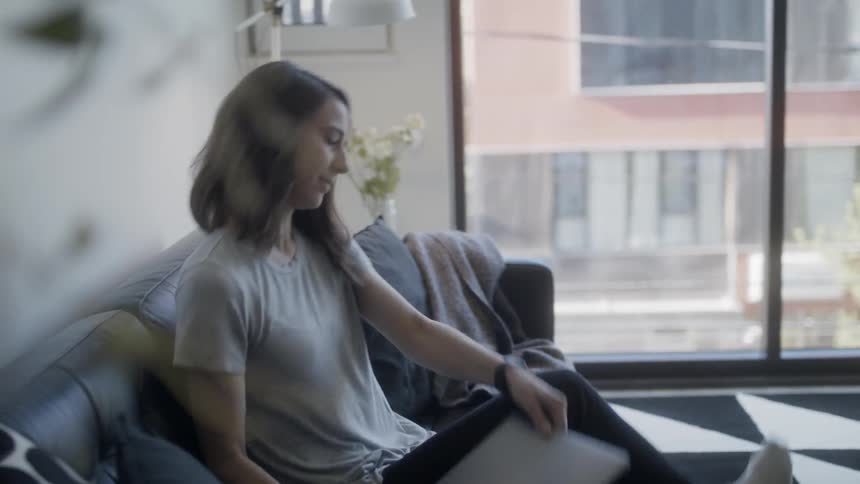 Woman sits down on a couch and opens a laptop