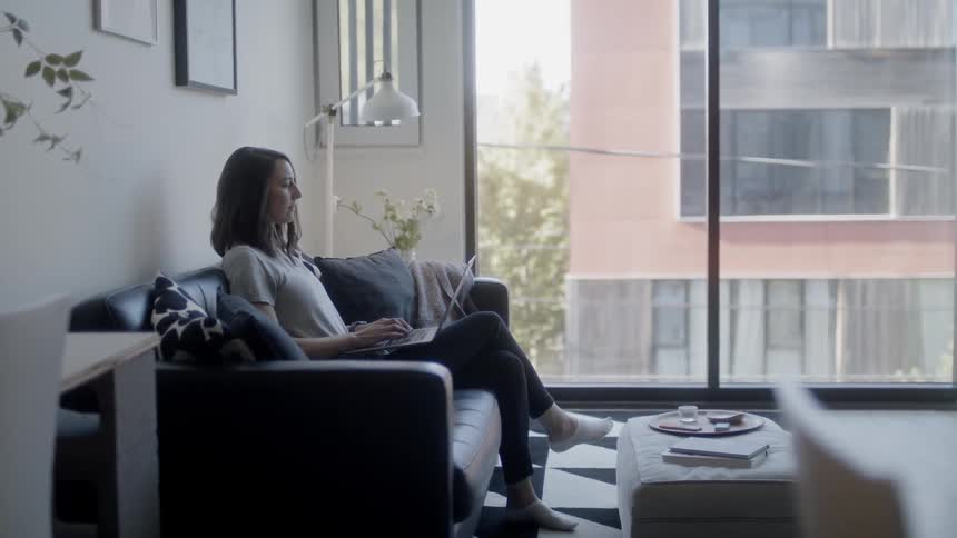 Woman sits on a sofa as she types on a laptop
