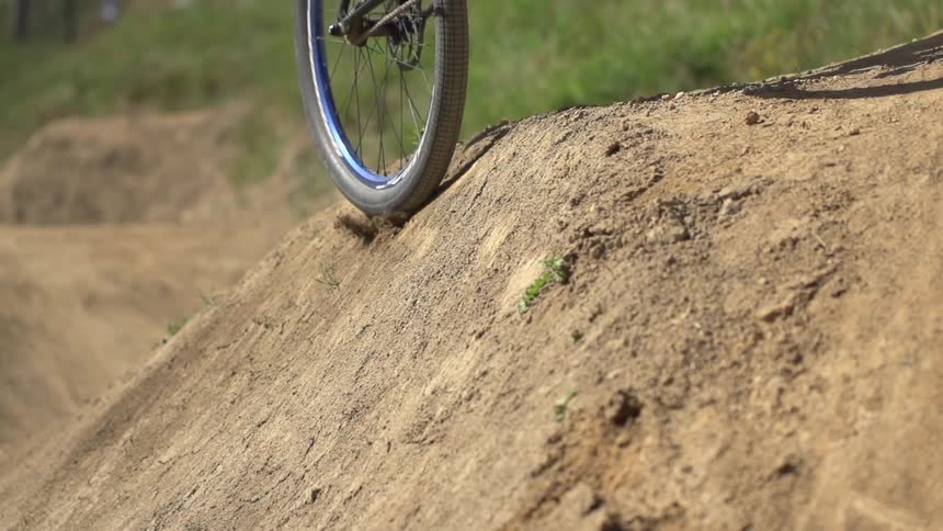 A young man riding his bicycle on a dirt hill as one wheel slips over the edge