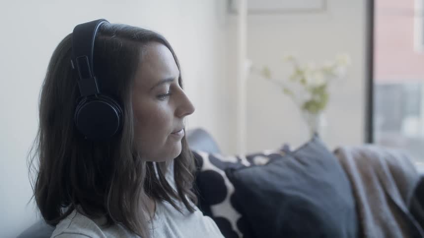 Woman sits on a couch with headphones on
