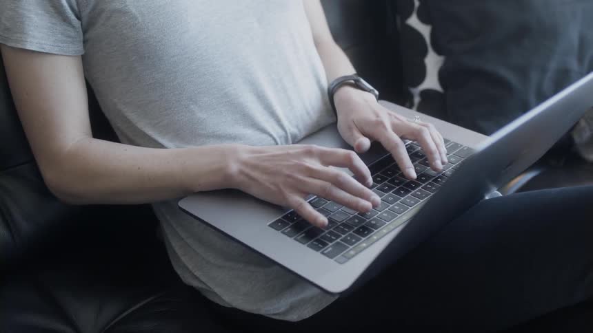 Person sits on a couch typing on a laptop