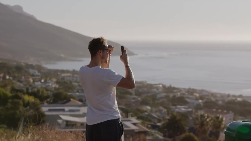 Man stands on a hilltop on a sunny day looking at his phone