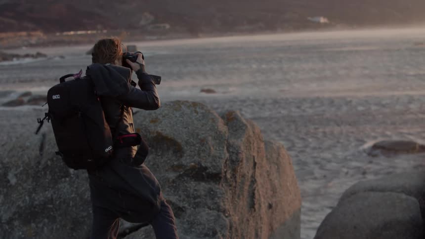 Man takes pictures of a body of water on a windy evening