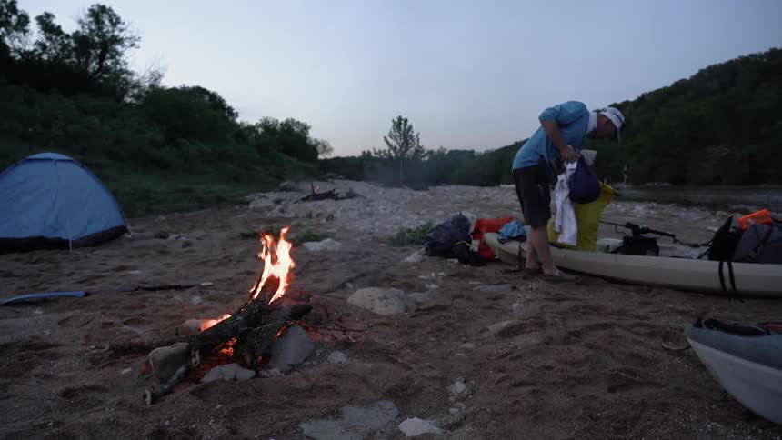 A man unpacks a bag near a campfire