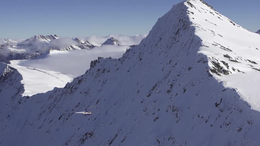 A helicopter flies near a snow-covered mountain peak