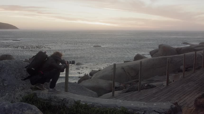 Man wearing a backpack takes a picture on the edge of a large body of water