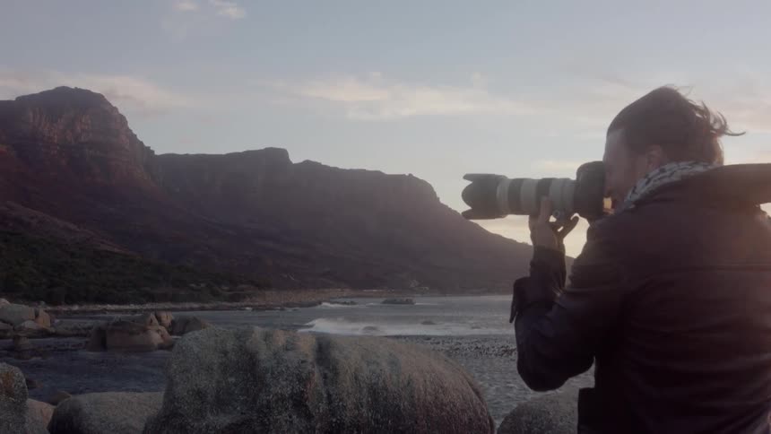 Man taking photographs by the ocean at sunset on windy evening