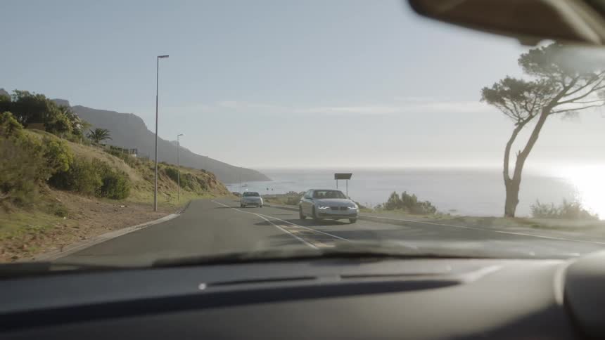Cars pass each other as they travel on a coast road on a sunny day