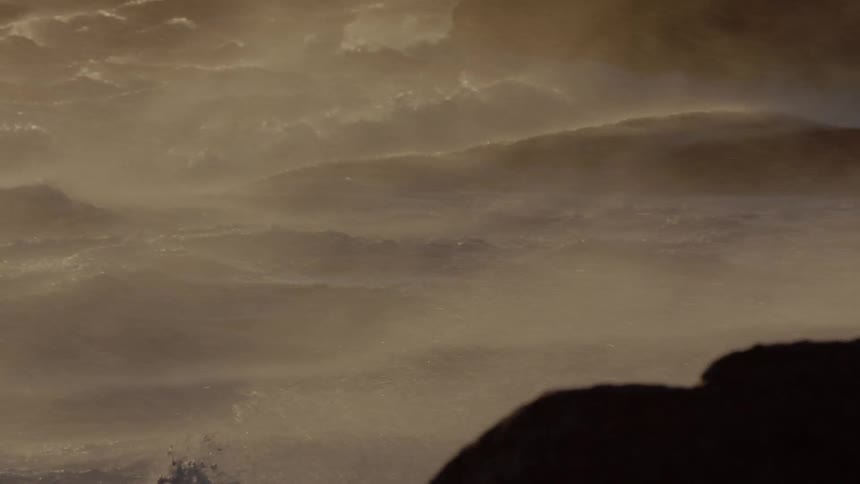 Water mists and splashes up on rocks on the beach at sunset