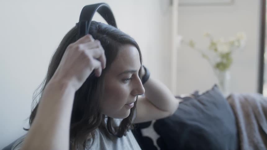 Woman sits on a couch and puts headphones on