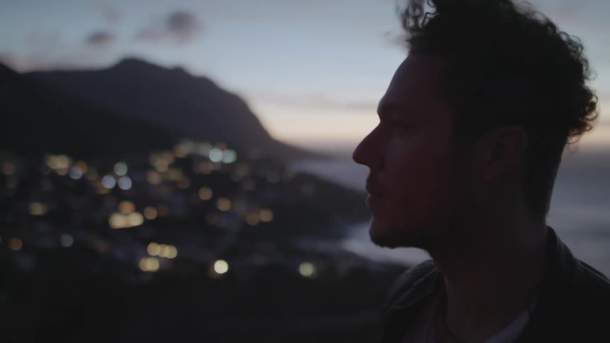 The wind is blowing a man's hair as he takes in a coastal view at dusk