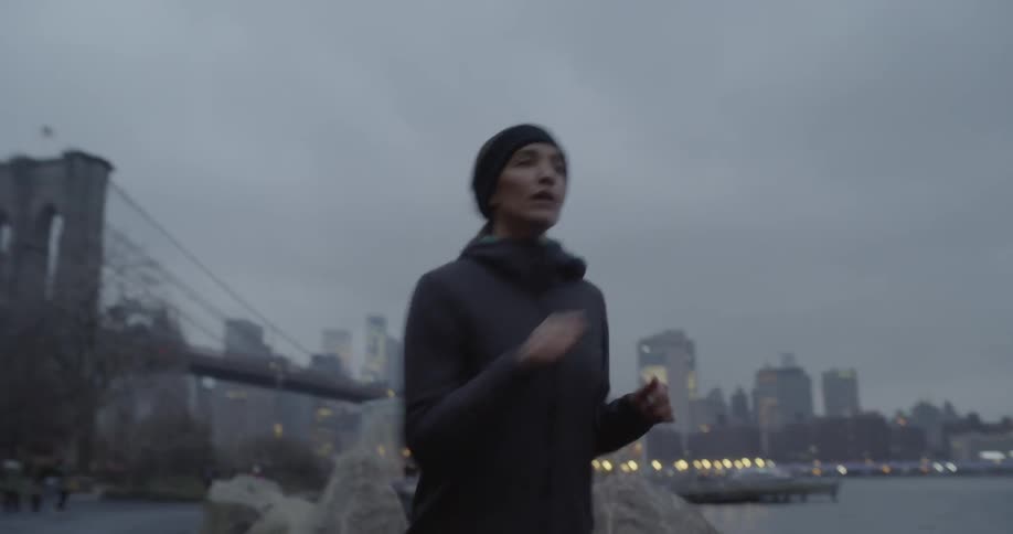 Woman jogs outside next to a river on a cloudy evening