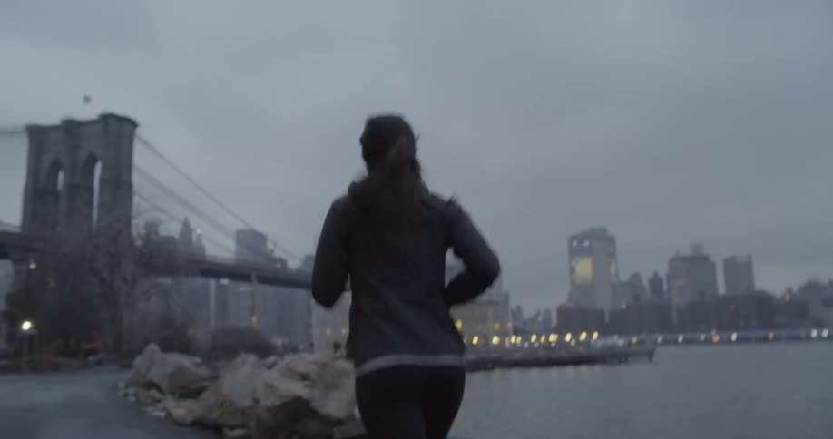 Woman jogs next to a river near a bridge in a city