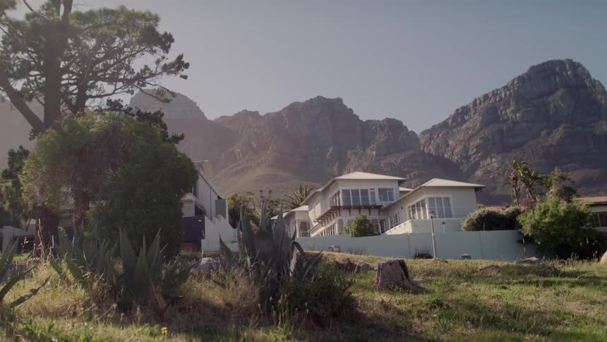Large white house sits near the mountains under a blue sky