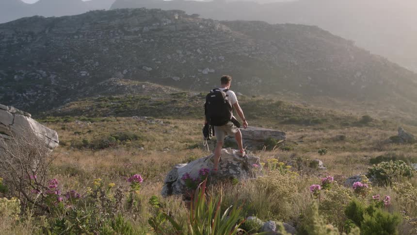 Man wearing a backpack climbs up onto a large rock