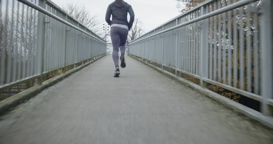 A woman jogs across a pedestrian bridge