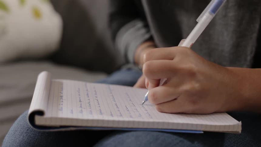 Woman writes in a notebook with a pen using her left hand