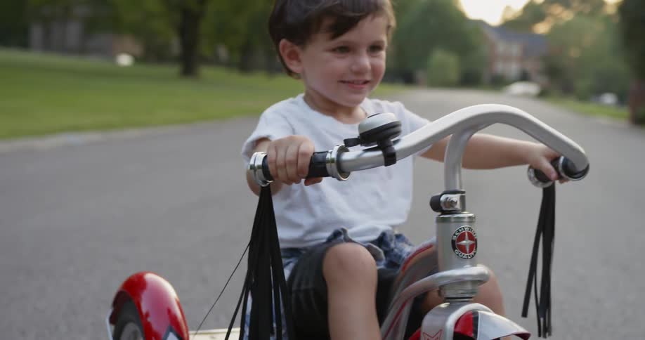 A boy rides a tricycle on a neighborhood road