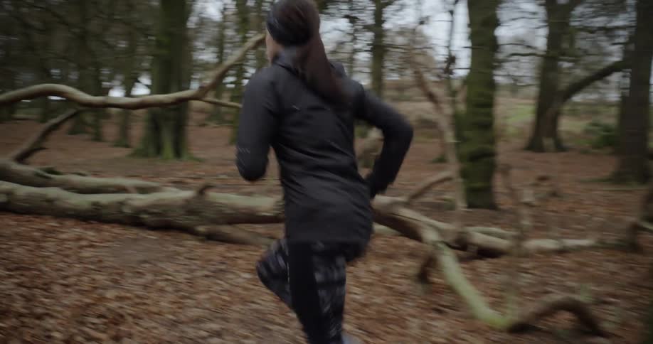 Woman jogs through the woods by a fallen tree
