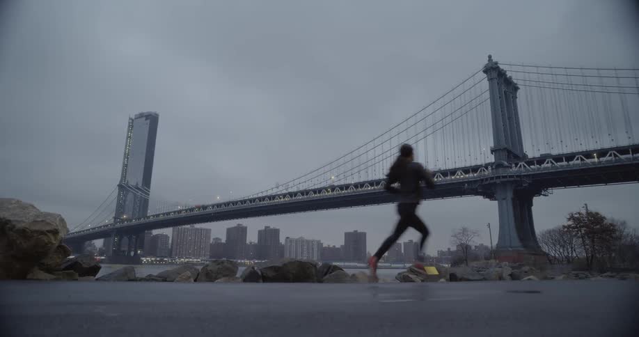 Woman runs on a sidewalk by a river on a cloudy day