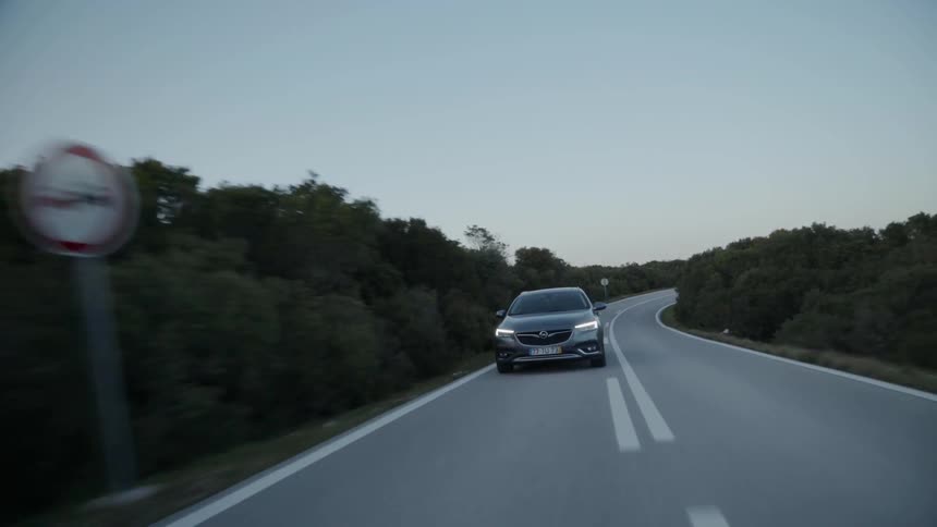 Car travels down the road that is lined with trees and rocks