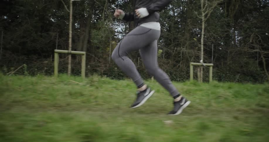 A woman is jogging on a dirt path near a wooded area in daylight