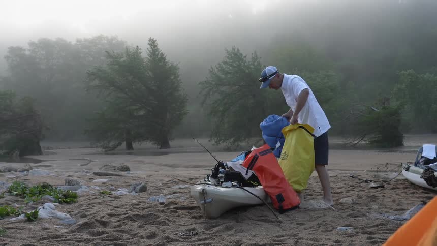 Man organizes bags on a kayak in the sand