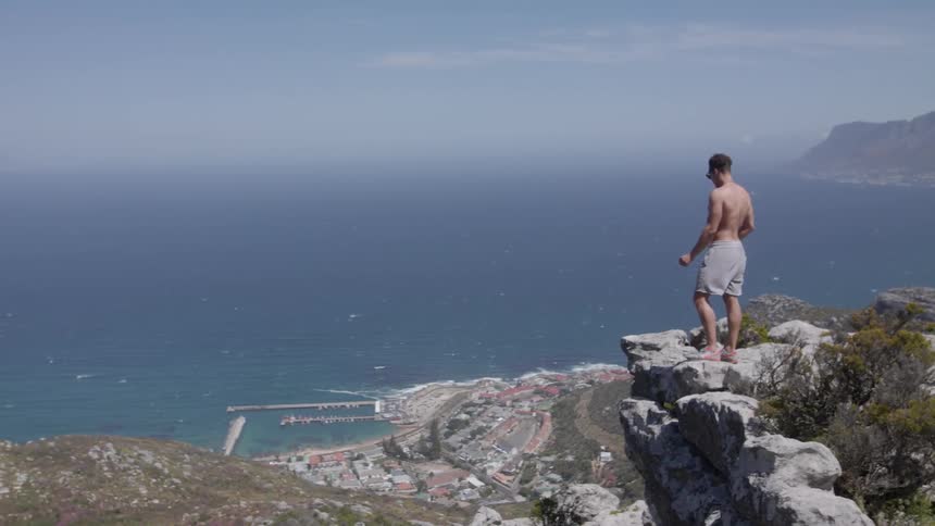 Man stands on a cliff overlooking a large body of water