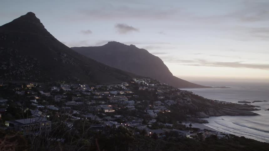 The lights of a coastal town at the base of a hill glow at sunset