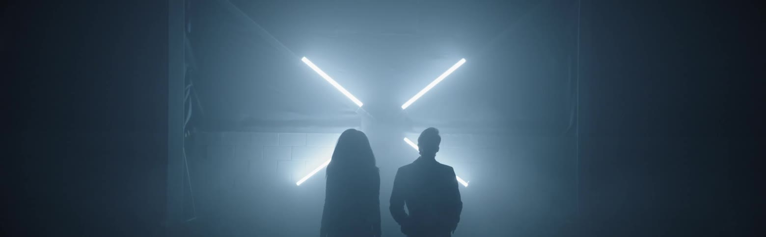 Man and woman stand on stage as colored lights flash