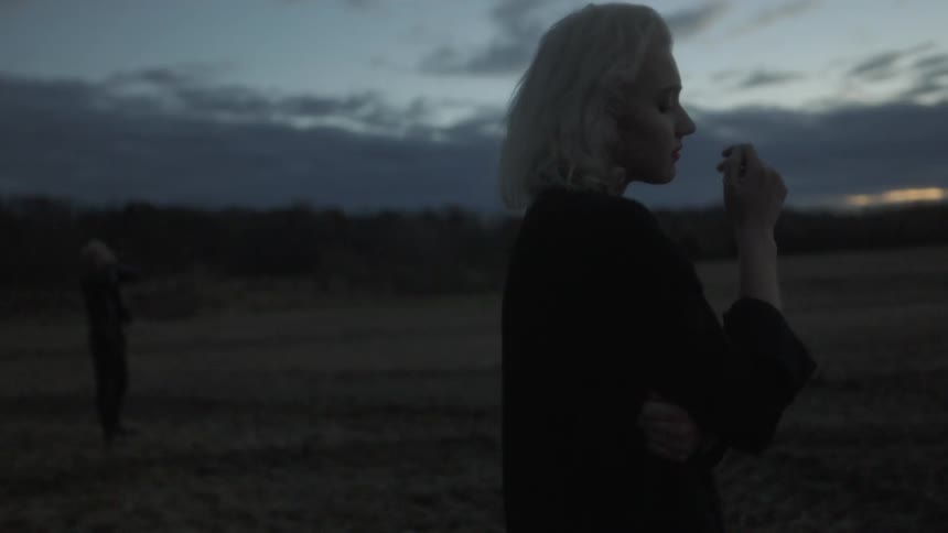 A woman looks back at a man in a field and covers her face